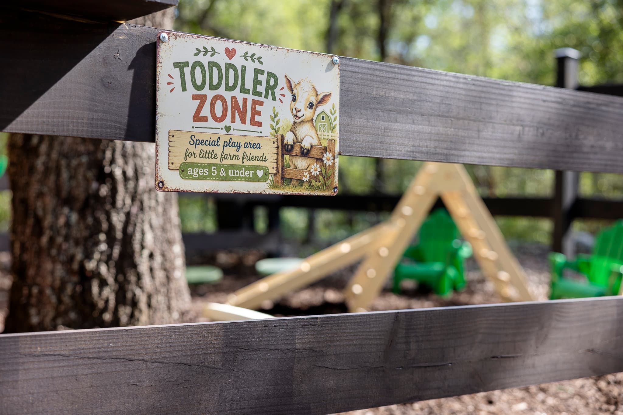 Rustic Toddler Zone sign with a goat illustration attached to a dark wooden fence.