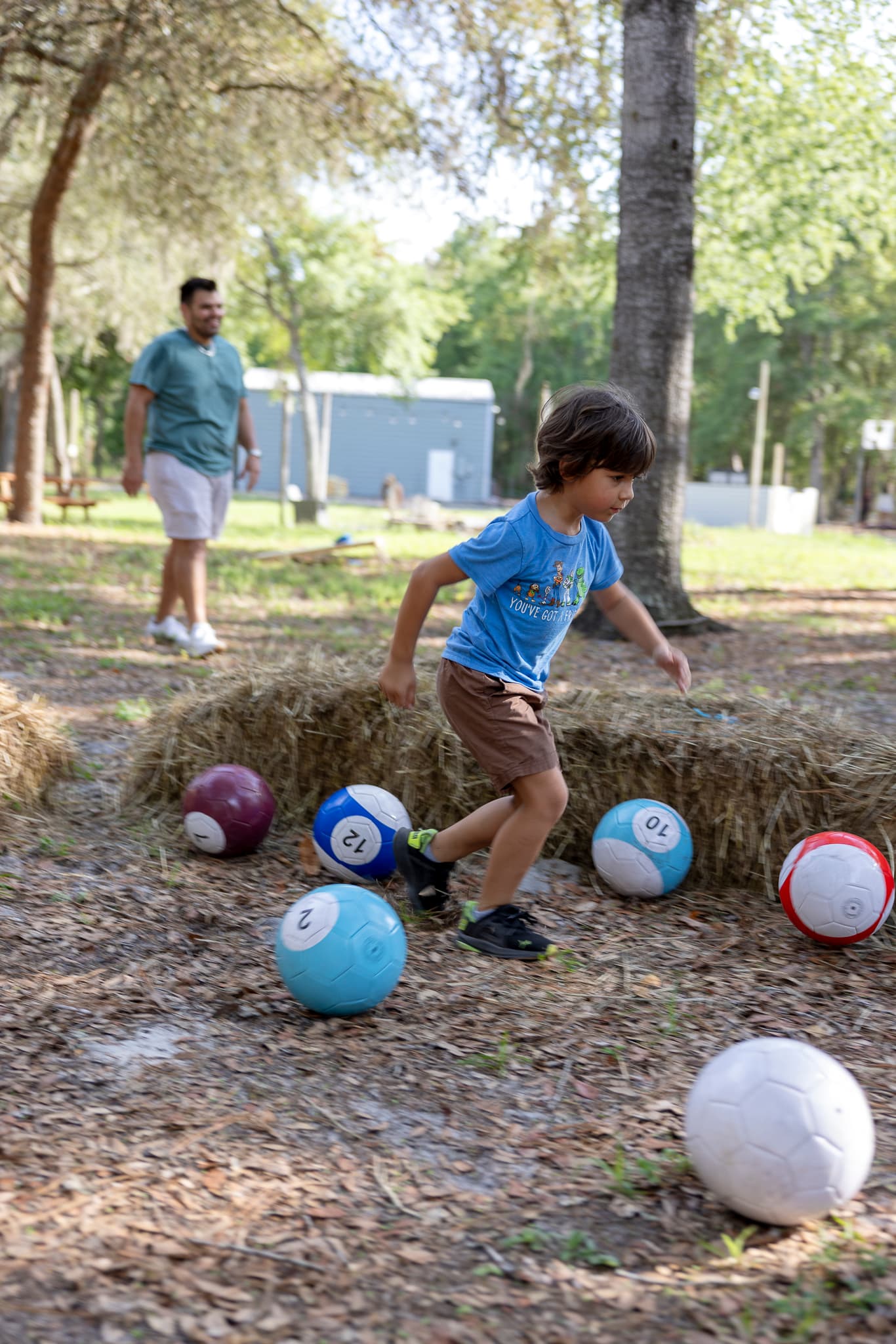 A young boy runs past colorful, numbered soccer balls styled like billiard balls outdoors.